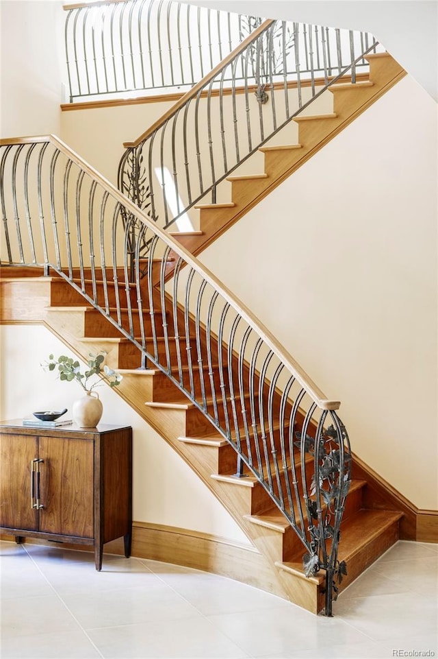stairway featuring a high ceiling, tile patterned flooring, and baseboards