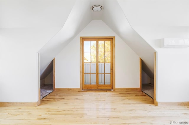 additional living space with lofted ceiling, wood finished floors, baseboards, and a wall unit AC