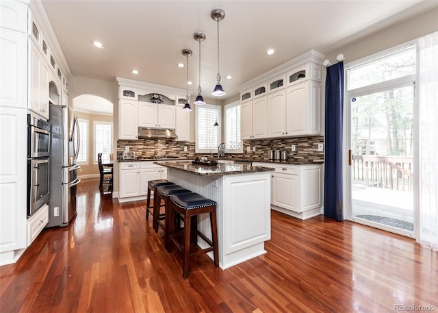 1530 Woodrose Ct, Colorado Springs, CO 80921 - kitchen featuring appliances with stainless steel finishes, arched walkways, dark wood finished floors, a kitchen island, and backsplash