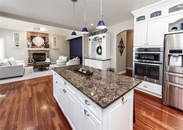 1530 Woodrose Ct, Colorado Springs, CO 80921 - kitchen featuring appliances with stainless steel finishes, ceiling fan, a stone fireplace, dark wood-type flooring, and arched walkways