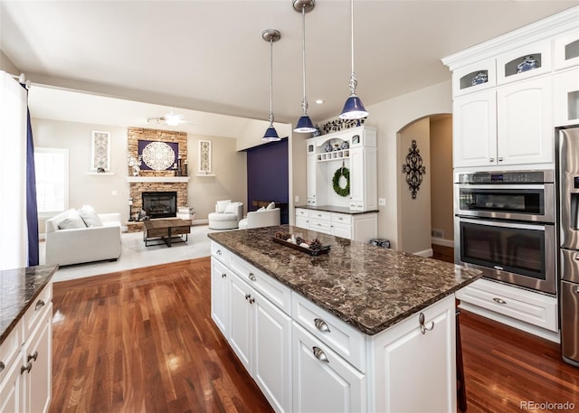 1530 Woodrose Ct, Colorado Springs, CO 80921 - kitchen featuring appliances with stainless steel finishes, a stone fireplace, a ceiling fan, arched walkways, and glass insert cabinets