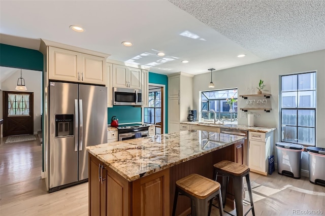 8820 W 80th Dr, Arvada, CO 80005 - kitchen featuring stainless steel appliances, a sink, light wood finished floors, light stone countertops, and a kitchen island