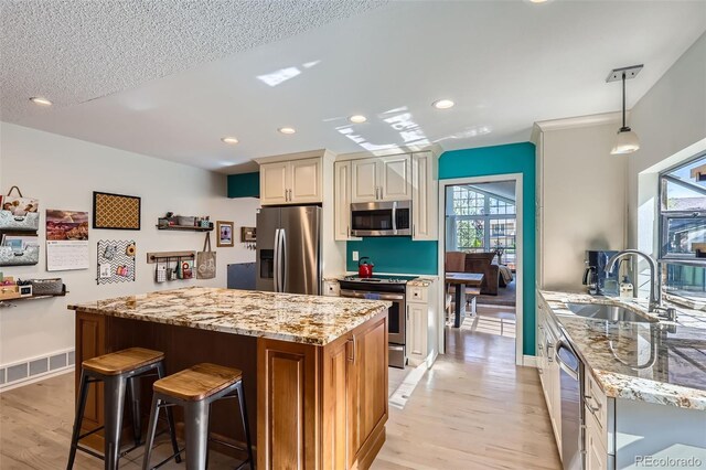 8820 W 80th Dr, Arvada, CO 80005 - kitchen with stainless steel appliances, a sink, light stone countertops, light wood finished floors, and a kitchen bar