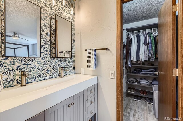 8820 W 80th Dr, Arvada, CO 80005 - bathroom with a textured ceiling, wood finished floors, a spacious closet, vanity, and ceiling fan