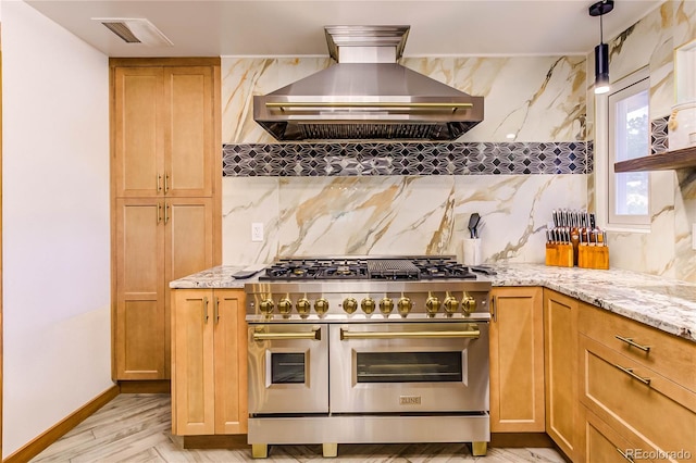 kitchen featuring light stone counters, wall chimney exhaust hood, range with two ovens, pendant lighting, and tasteful backsplash