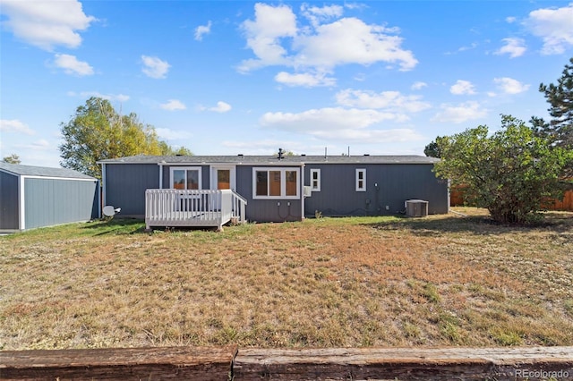 rear view of property featuring a wooden deck, central AC, a lawn, and an outbuilding