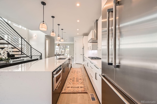 427 Milwaukee St, Denver, CO 80206 - kitchen featuring a sink, wall chimney exhaust hood, stainless steel appliances, white cabinetry, and visible vents