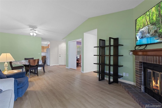 living room with light wood finished floors, a ceiling fan, a fireplace, lofted ceiling, and baseboards