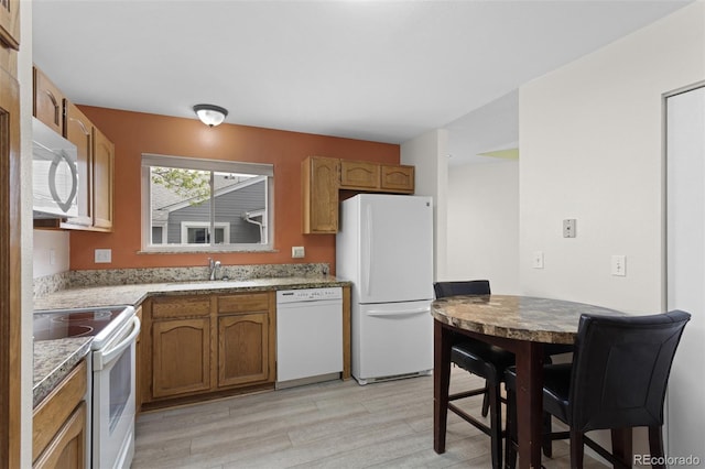 kitchen with white appliances, light wood finished floors, brown cabinetry, and a sink