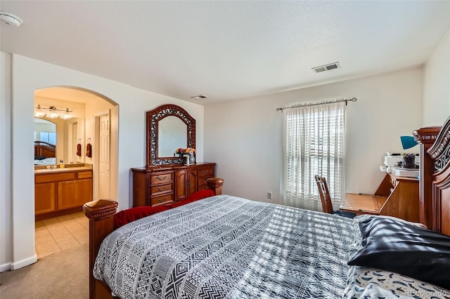 bedroom with ensuite bath, visible vents, arched walkways, and light colored carpet