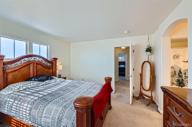 bedroom with arched walkways, baseboards, and light colored carpet