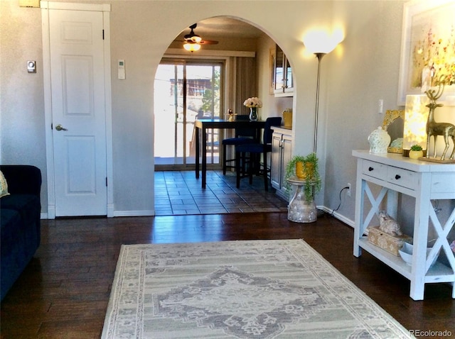 interior space featuring arched walkways, dark wood-style flooring, ceiling fan, and baseboards