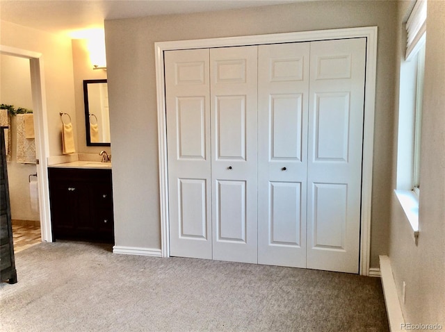 unfurnished bedroom with light carpet, a closet, a sink, and ensuite bathroom