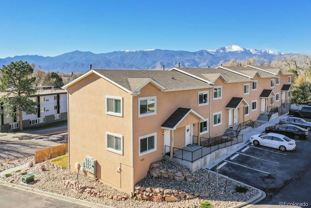 view of front of home featuring uncovered parking, a mountain view, fence, stucco siding, and a residential view