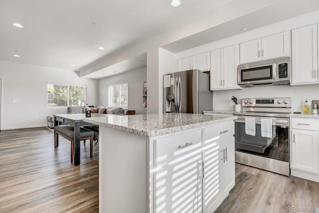kitchen featuring open floor plan, light wood-type flooring, stainless steel appliances, white cabinetry, and a kitchen island