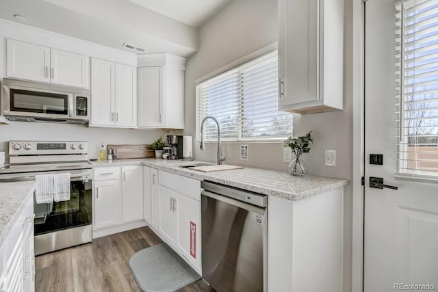kitchen featuring white cabinets, stainless steel appliances, light wood-style flooring, a sink, and visible vents