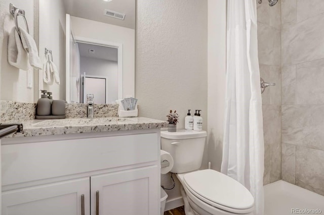 bathroom featuring a tile shower, toilet, vanity, and visible vents