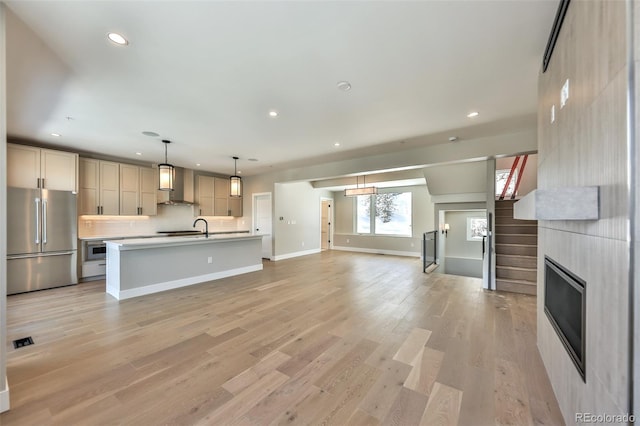 kitchen with an island with sink, light hardwood / wood-style floors, decorative backsplash, hanging light fixtures, and high end fridge