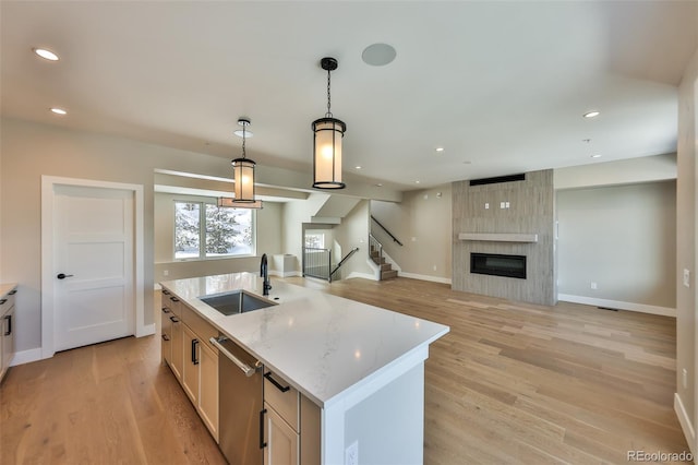 kitchen featuring dishwasher, hanging light fixtures, sink, light stone counters, and an island with sink