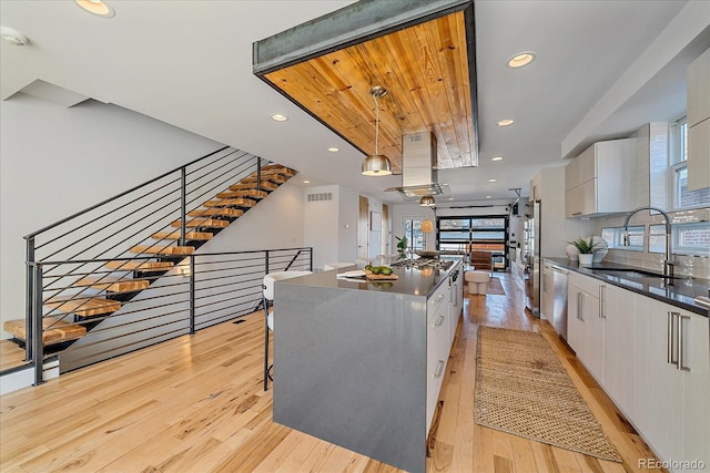 kitchen with white cabinets, dark countertops, modern cabinets, a center island, and island exhaust hood