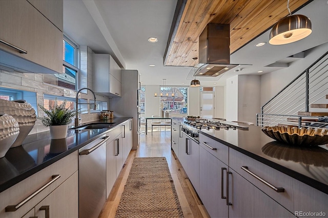 kitchen featuring a sink, light wood-type flooring, backsplash, dark countertops, and island exhaust hood