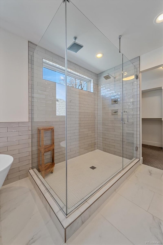 bathroom with a stall shower, marble finish floor, tile walls, and recessed lighting