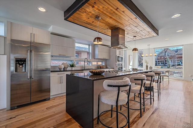 kitchen with stainless steel appliances, a breakfast bar, ventilation hood, dark countertops, and modern cabinets