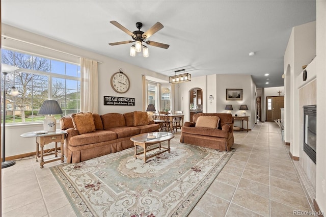 22312 E Plymouth Cir, Aurora, CO 80016 - living area featuring arched walkways, ceiling fan, light tile patterned flooring, baseboards, and a glass covered fireplace