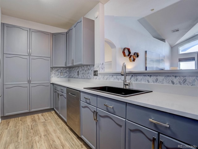 kitchen featuring sink, gray cabinetry, vaulted ceiling, stainless steel dishwasher, and light wood-type flooring