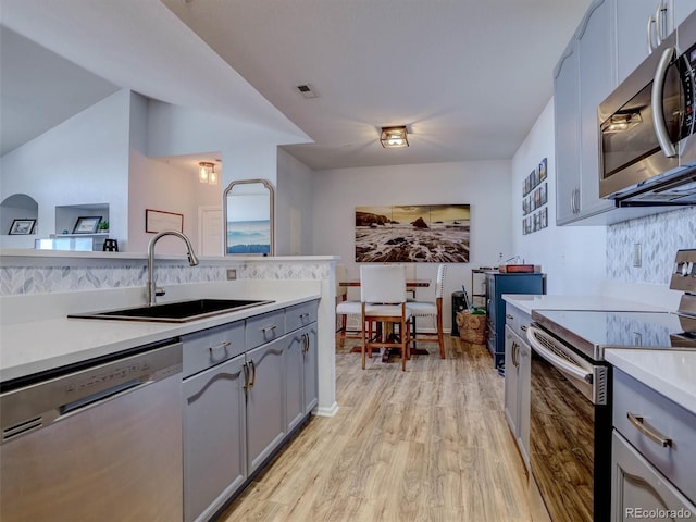 kitchen featuring light wood-type flooring, stainless steel appliances, sink, and gray cabinetry