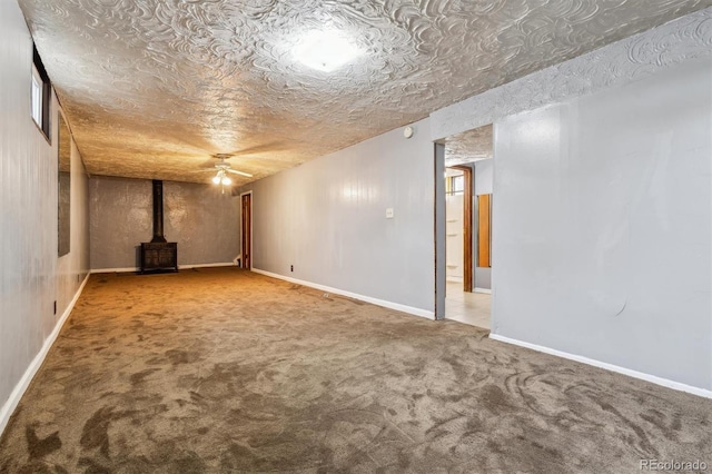 basement with a wood stove, ceiling fan, carpet floors, and a textured ceiling