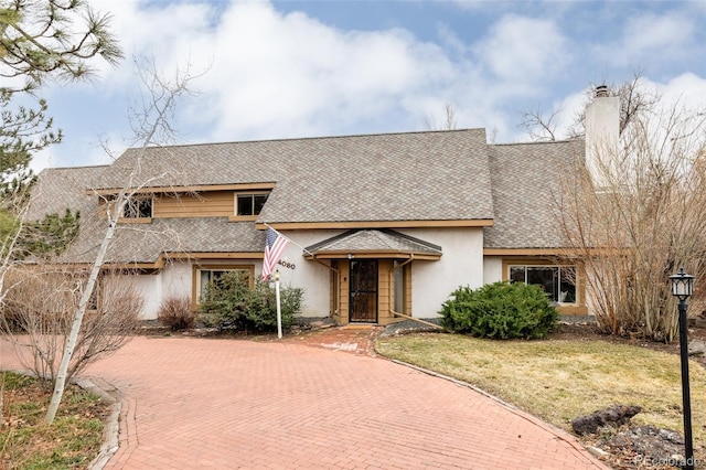 view of front of property featuring stucco siding, a front lawn, decorative driveway, roof with shingles, and a chimney