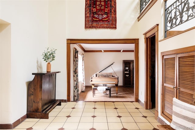 corridor featuring light tile patterned floors, baseboards, and a towering ceiling