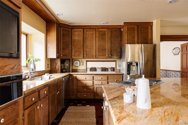 kitchen with light stone counters, brown cabinetry, appliances with stainless steel finishes, and a sink