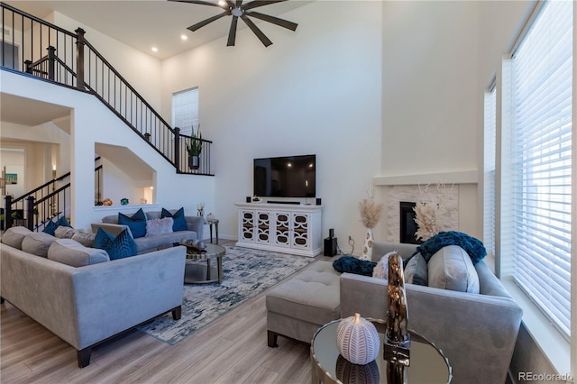 living room featuring a glass covered fireplace, plenty of natural light, stairway, and wood finished floors