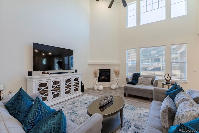 living room featuring a high ceiling, a fireplace, wood finished floors, and a ceiling fan