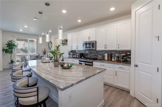 kitchen with stainless steel appliances, a kitchen island, white cabinetry, decorative backsplash, and light stone countertops