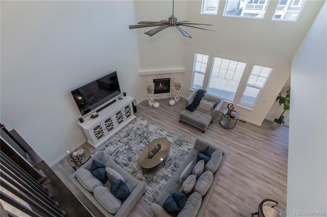 living room with baseboards, a towering ceiling, ceiling fan, wood finished floors, and a fireplace