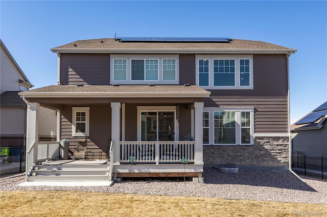 back of property featuring covered porch, roof with shingles, and roof mounted solar panels