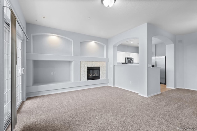 12711 Colorado Blvd Unit 1116, Thornton, CO 80241 - unfurnished living room with light carpet, baseboards, a glass covered fireplace, arched walkways, and plenty of natural light