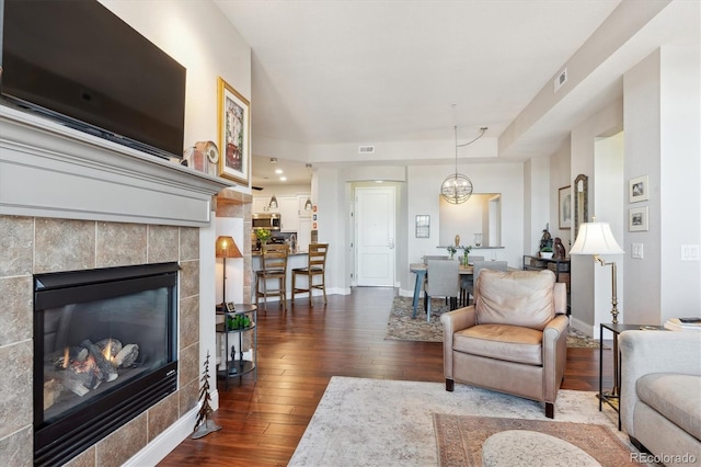 living room featuring a tiled fireplace and dark wood-type flooring