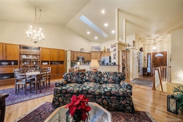 living room featuring a chandelier, light hardwood / wood-style floors, high vaulted ceiling, and a skylight