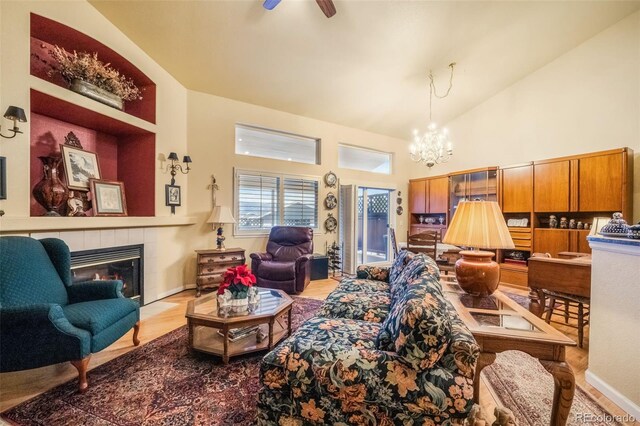 living room featuring hardwood / wood-style floors, high vaulted ceiling, ceiling fan with notable chandelier, and a tile fireplace