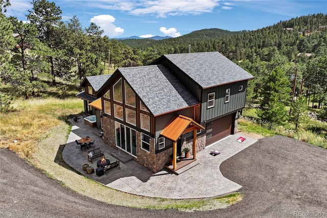 518 Conifer Dr, Bailey, CO 80421 - rear view of property featuring stone siding, roof with shingles, a wooded view, a fire pit, and driveway