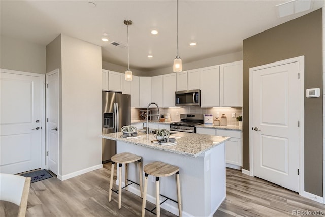 kitchen featuring appliances with stainless steel finishes, light stone counters, a kitchen island with sink, sink, and white cabinetry