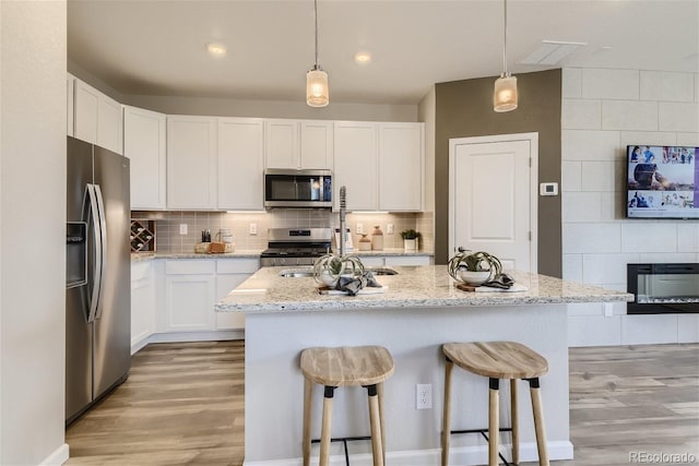 kitchen with white cabinetry, light stone countertops, stainless steel appliances, pendant lighting, and a kitchen island with sink