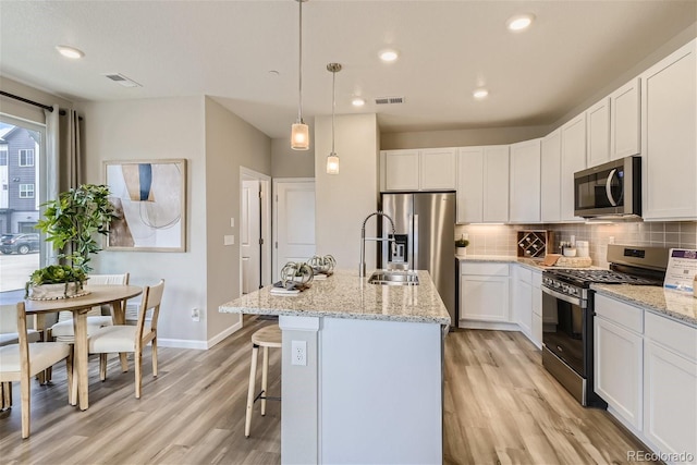 kitchen featuring pendant lighting, a kitchen island with sink, light stone counters, white cabinetry, and stainless steel appliances