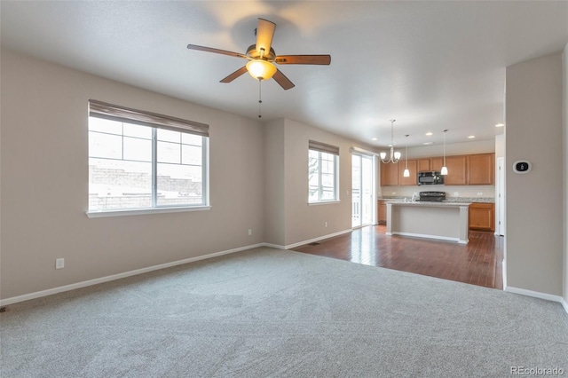 unfurnished living room featuring ceiling fan with notable chandelier, dark colored carpet, recessed lighting, and baseboards