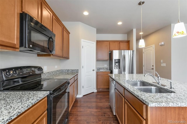 kitchen featuring brown cabinets, a center island with sink, hanging light fixtures, a sink, and black appliances