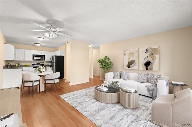 720 S Clinton St Unit 1B, Denver, CO 80247 - living room featuring light wood-style flooring, a ceiling fan, a textured ceiling, and baseboards